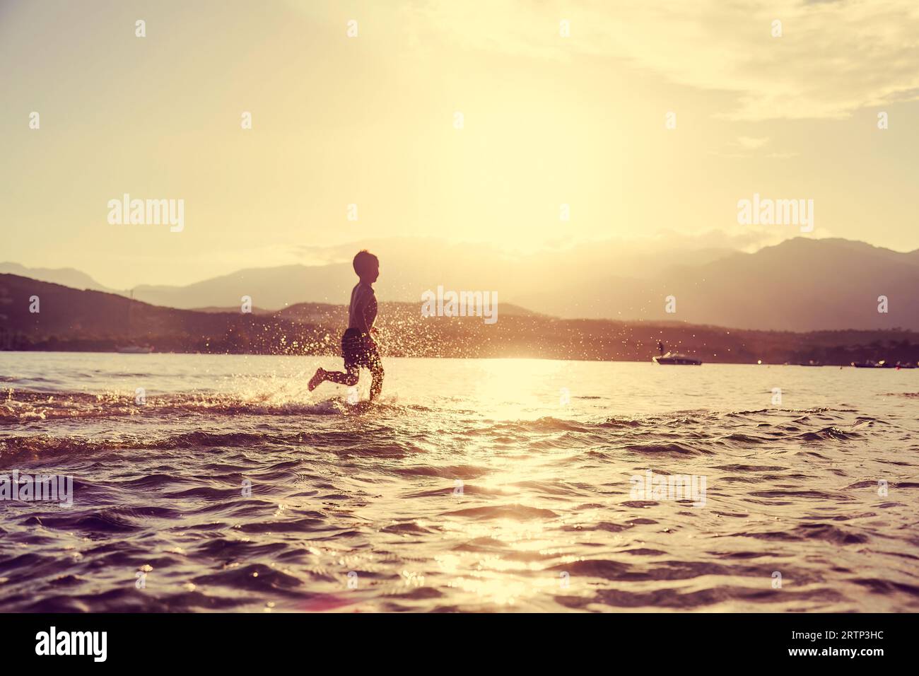 Der kleine Junge rennt bei Sonnenuntergang glücklich ins Meer Stockfoto