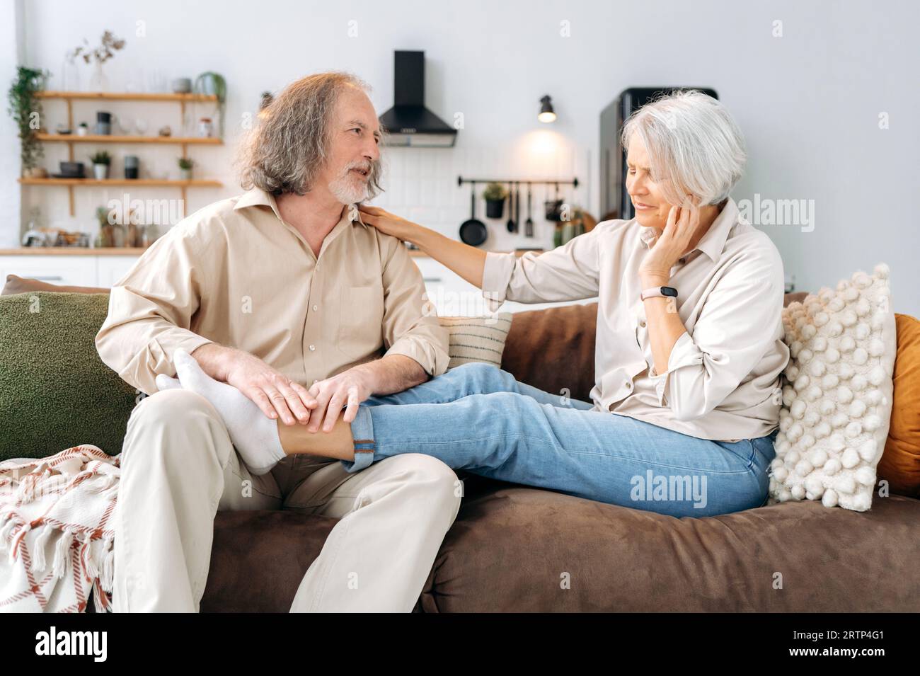 Kaukasische, grauhaarige Rentner, reifer Ehemann und Ehefrau, verbringen Zeit zusammen zu Hause auf dem Sofa im Wohnzimmer, Mann massiert seine geliebte Ehefrau Füße, sie ruhen sich aus und entspannen sich zusammen Stockfoto