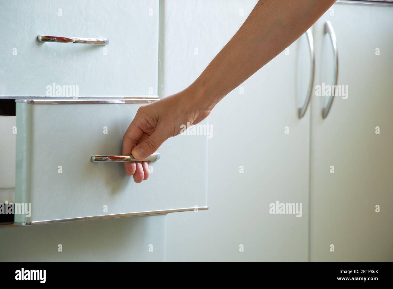 Die Hand der Frau öffnet den Küchenschrank unter Sonnenlicht, Küchenmöbel zu Hause Stockfoto