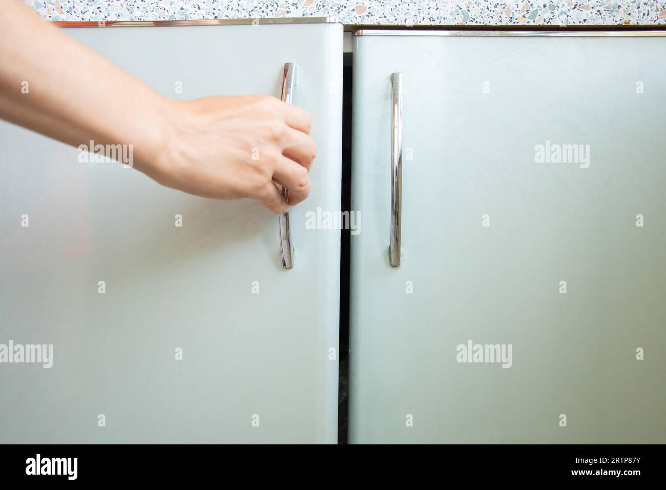 Die Hand der Frau öffnet den Küchenschrank unter Sonnenlicht, Küchenmöbel zu Hause Stockfoto
