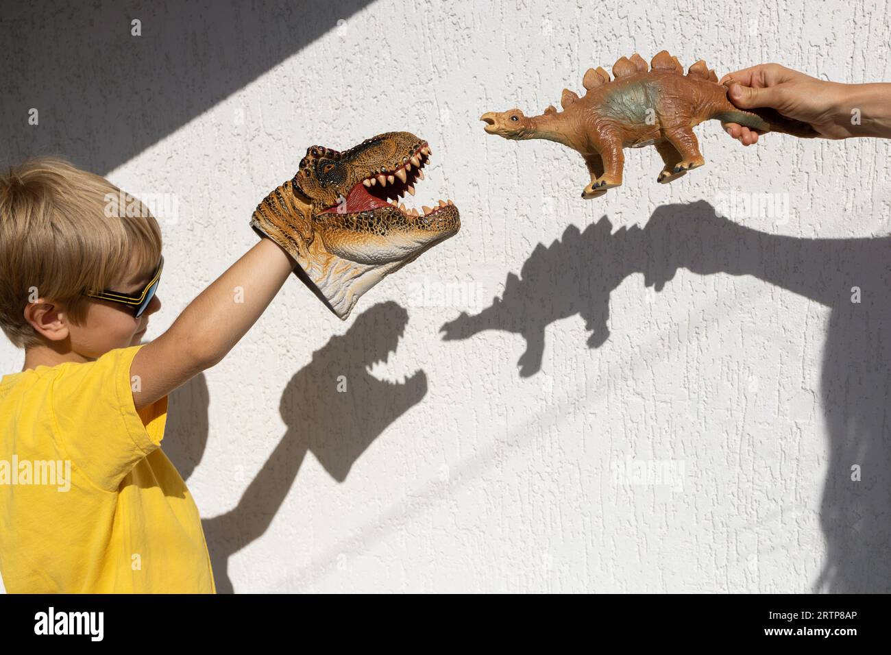 Junge und Mutter spielen mit dem Spielzeug-Dinosaurier und erzeugen interessante, kontrastreiche Schatten an der Wand. Ein sonniger Tag. Glückliche, fröhliche Kindheit, Ideen Stockfoto