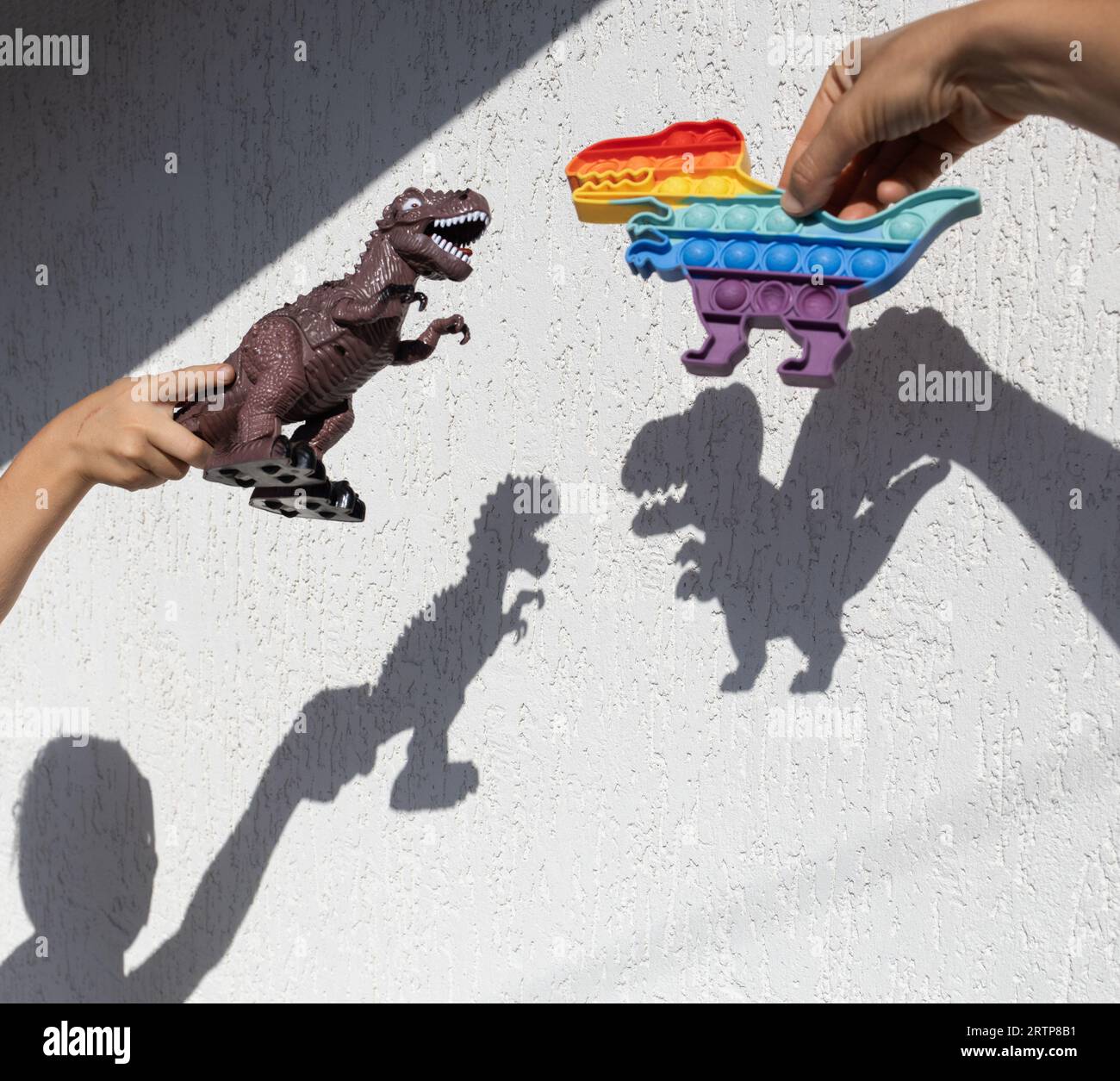 Dinosaurier-Spielzeuge zeigen interessante, kontrastierende Schatten an einer hellen Wand. Ein sonniger Tag. Fröhliche Kindheit, Ideen für Spiele, Lifestyle Stockfoto