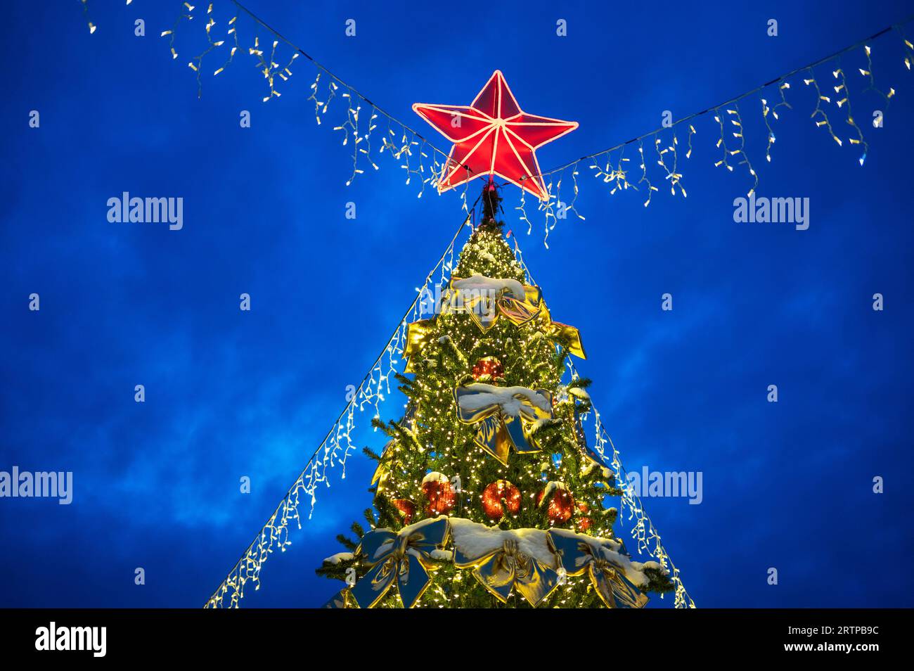 Weihnachtsbaum mit rotem Stern oben auf der Abendstraße. Silvesterabend oder Weihnachtsdekoration auf der Straße am Abend in der Stadt Stockfoto