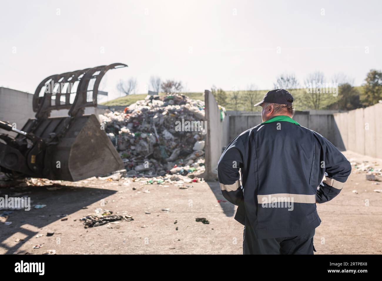 Ein Mitarbeiter des Recyclingzentrums in dunkelblauer Arbeitskleidung, der sich einen unsortierten Müllhaufen ansieht, ist gerade in der Materialrückgewinnungsanlage eingetroffen Stockfoto