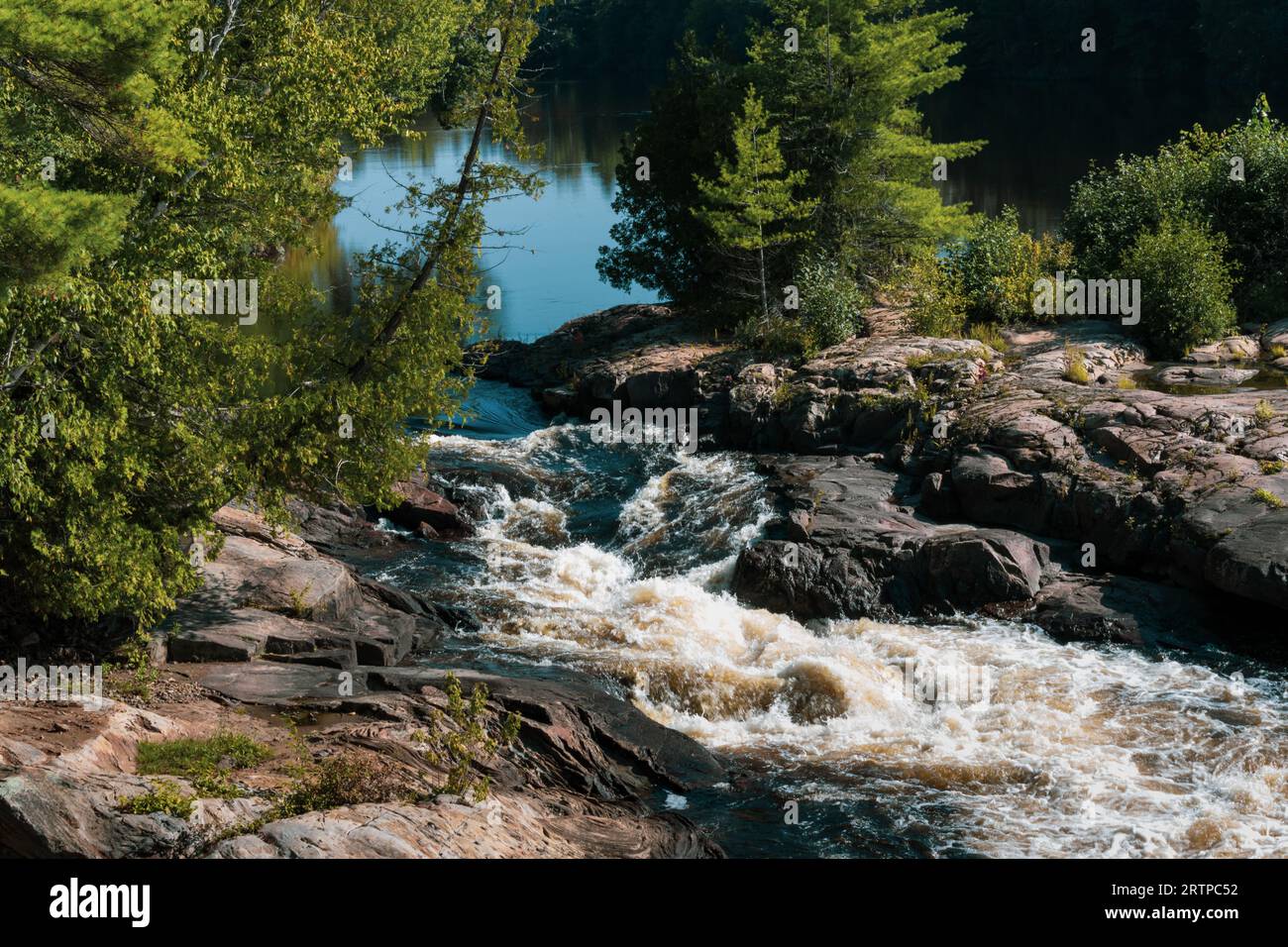 Das Wasser fließt von der Ruhe zu Stromschnellen, wenn es auf ein felsiges Flussbett trifft Stockfoto