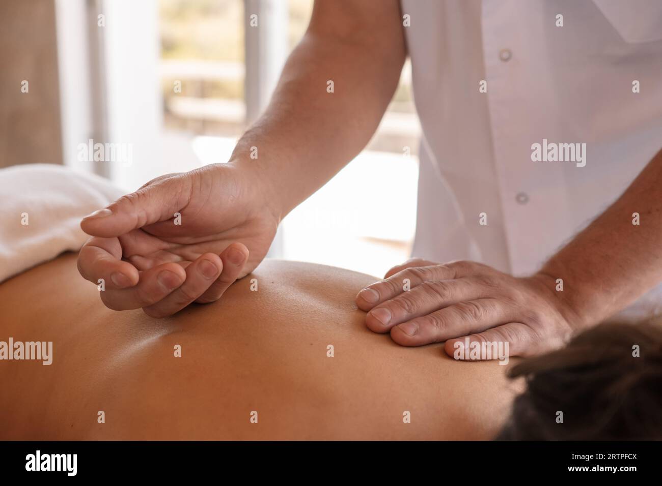 Detailaufnahme der Hände eines Masseurs, der den Rücken einer Frau behandelt, die auf einem Massagetisch in einer Klinik liegt. Stockfoto