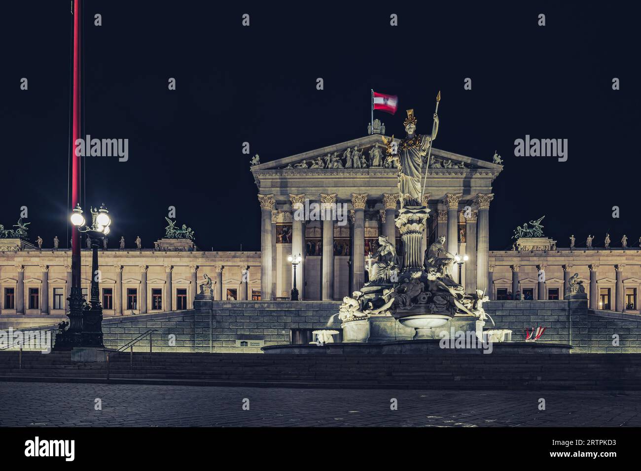 Wien, Österreich. Blick auf das Wiener parlamentsgebäude, das nachts beleuchtet wird, mit der schwenkenden österreichischen Flagge und dem Pallas-athene-Brunnen im Stockfoto