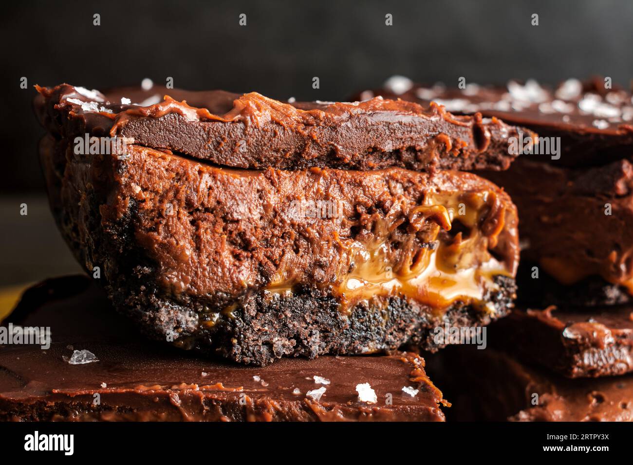 Karamell-Schokoladen-Käsekuchen-Dessertstangen mit Ganache-Belag: Schichten von Schokoladenkruste, Karamell, Käsekuchenfüllung und dunkler Schokoladenganache Stockfoto