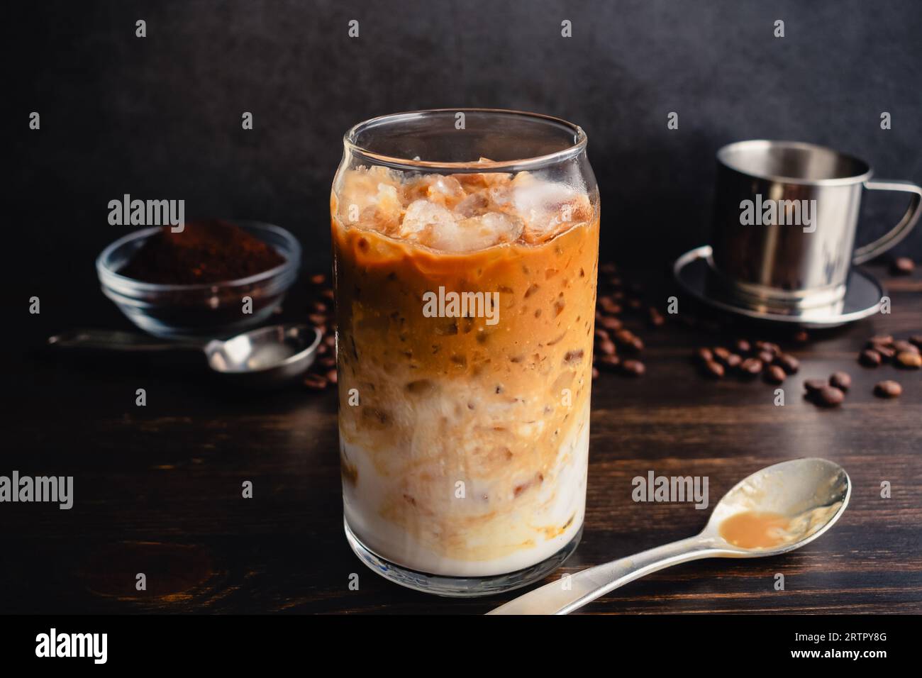 Vietnamesischer Joghurtkaffee (Sua Chua Cafe oder Cà Phê Sữa): Ein Glas vietnamesischer Eiskaffee mit gespritztem Joghurt mit Löffel und phin-Filter Stockfoto