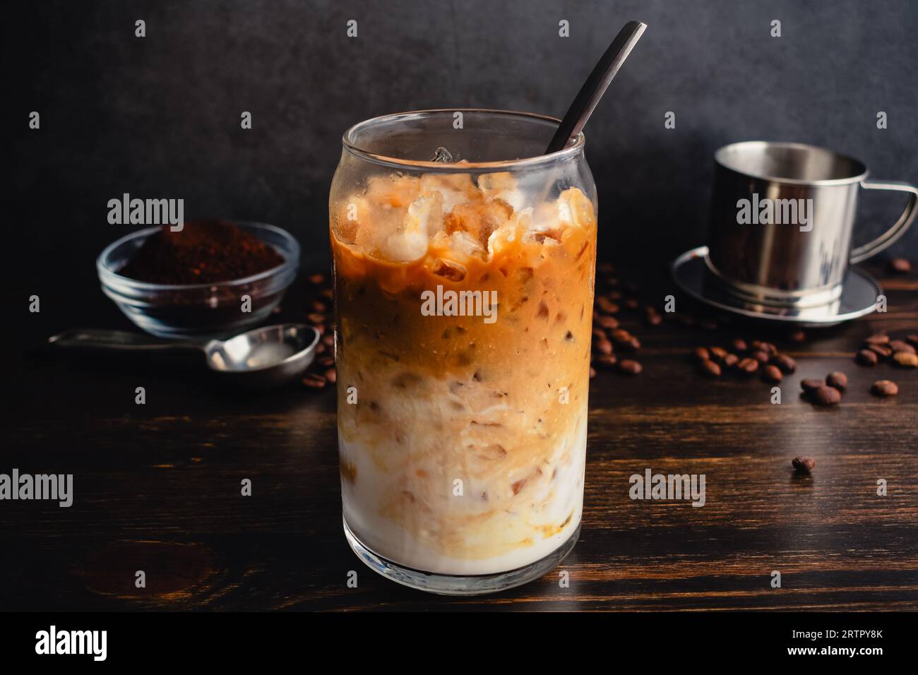 Vietnamesischer Joghurtkaffee (Sua Chua Cafe oder Cà Phê Sữa): Ein Glas vietnamesischer Eiskaffee mit gespritztem Joghurt mit Löffel und phin-Filter Stockfoto