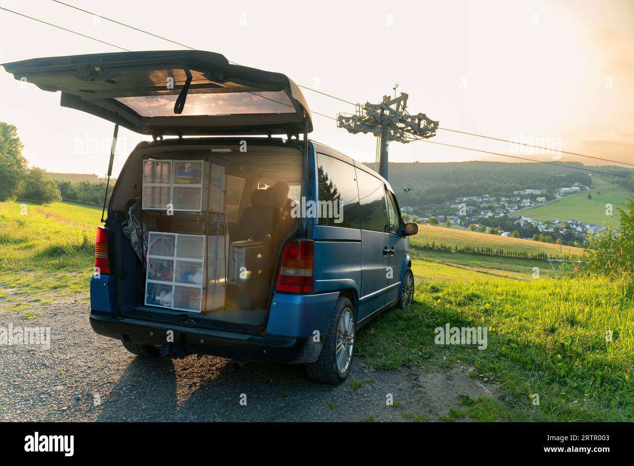 Vanlife. Blauer Van parkte vor einer wunderschönen Aussicht im Willinger Upland in Deutschland. Neben dem Fahrzeug befindet sich ein Skilift. Der Kofferraum ist offen. Hausgemachte s Stockfoto