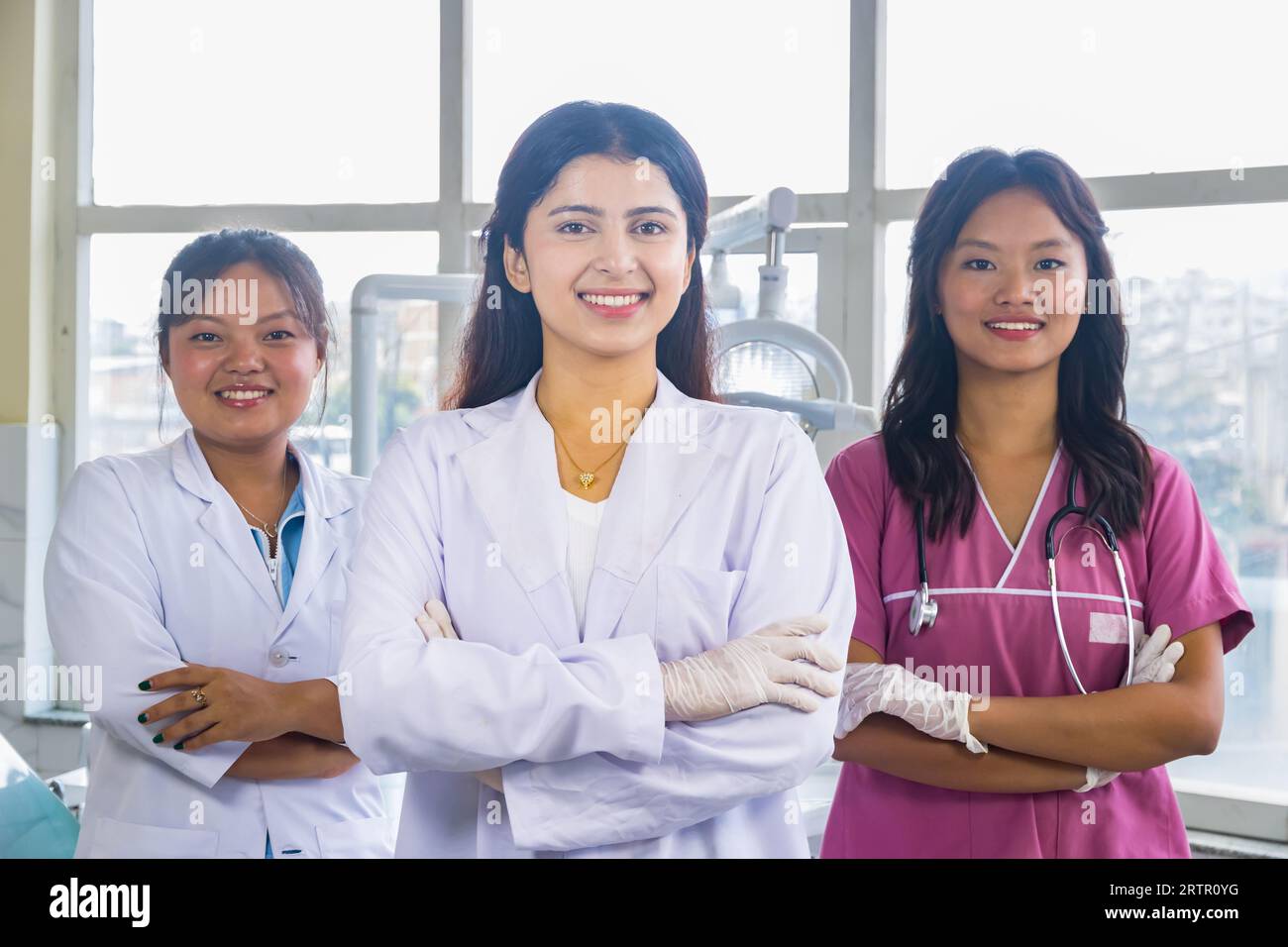 Selbstbewusste Gruppe von nepalesischen indischen Krankenschwestern und Ärzten, die mit überkreuzten Händen in einem Zahnklinikum lächeln Stockfoto