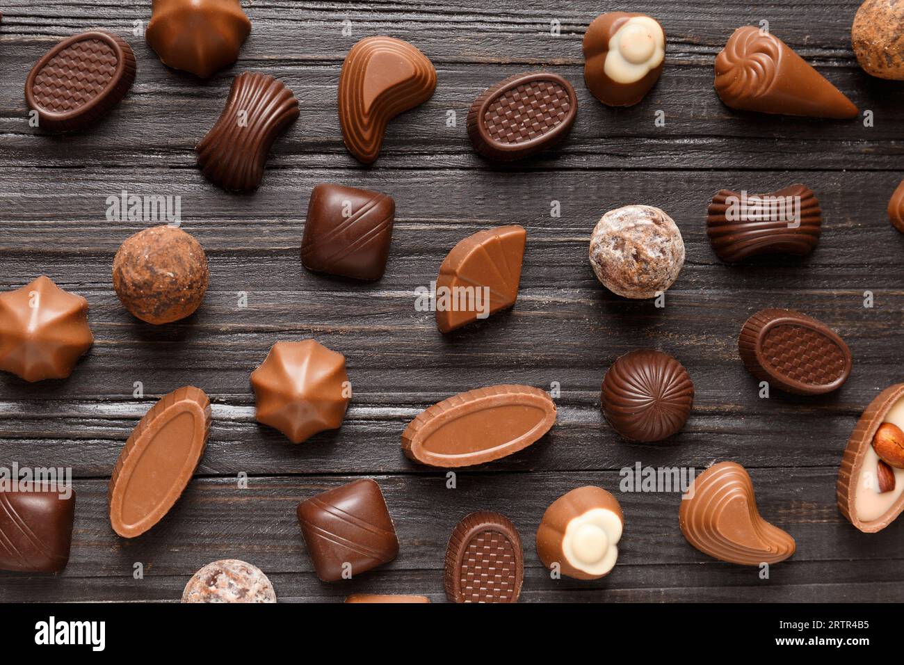 Verschiedene Schokoladenbonbons auf dunklem Holzhintergrund, Draufsicht. Verschiedene Süßigkeiten auf dem Tisch. Dunkle Schokolade und Milchschokolade. Schokoladendessert. Stockfoto