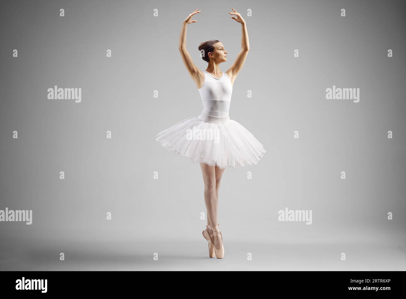 Ballerina in einem weißen Kleid tanzt mit den Armen isoliert auf grauem Hintergrund Stockfoto