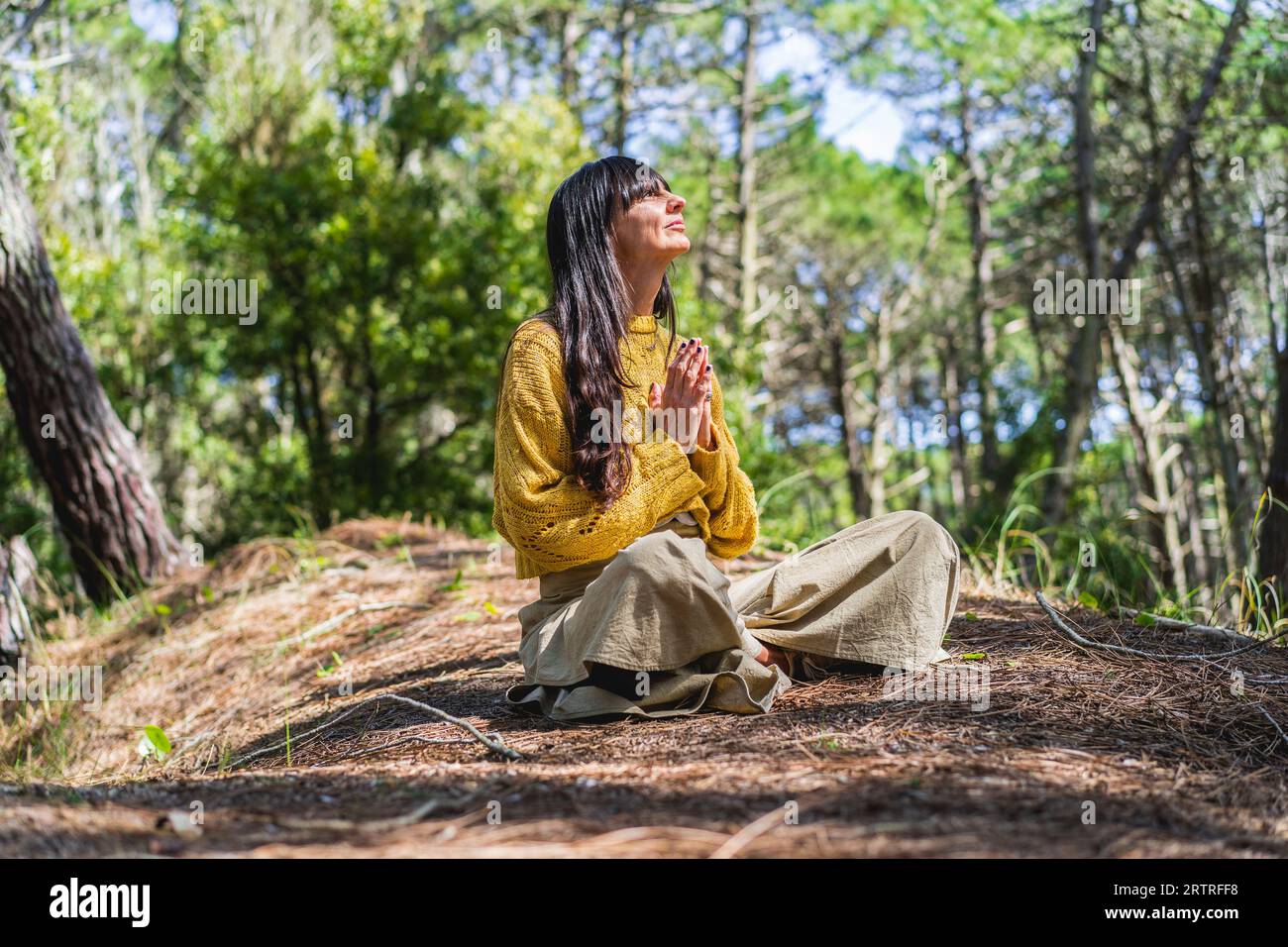 Frau, die gerade meditiert, mit gefalteten Händen, die in den Wald blicken Stockfoto