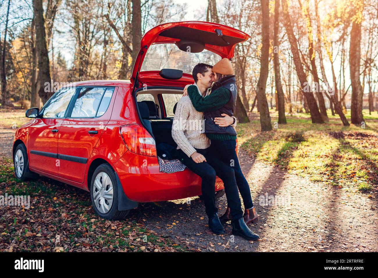 Glückliches, liebevolles Paar, das sich im Autokoffer im Herbstwald entspannt. Mann und Frau reisen im Auto und tragen warme Kleidung. Junge Leute genießen Herbstreise. S Stockfoto
