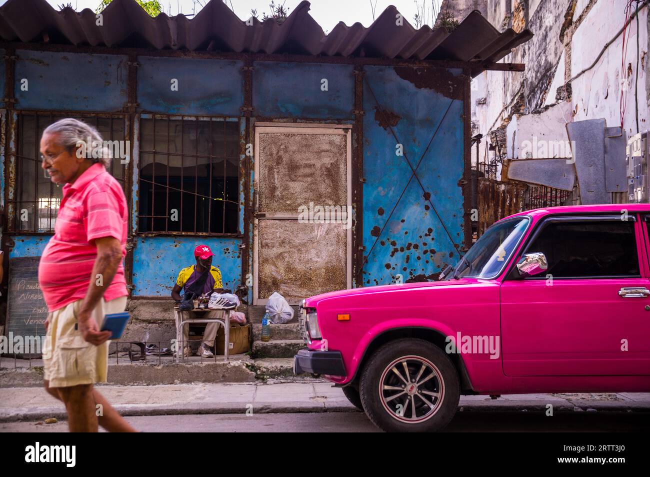 Havanna, Kuba am 23. Dezember 2015: ein Mann geht auf eine Straße in Centro Habana mit seinem Hemd Farbe von rosa Oldtimer Stockfoto