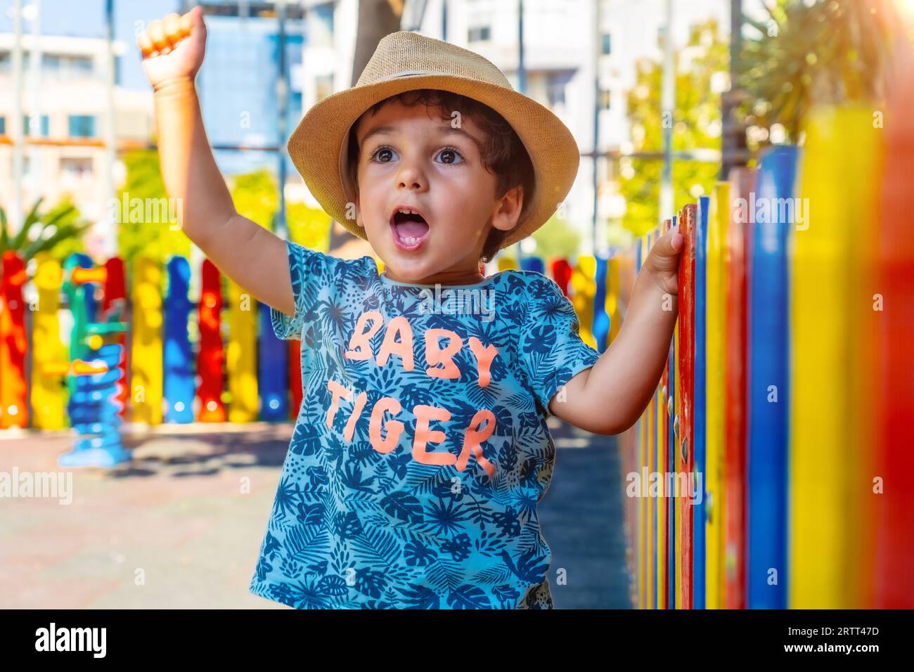 Porträt eines glücklichen kleinen Jungen im Hut, der auf dem Spielplatz spielt und die Hand hebt, um etwas zu feiern Stockfoto