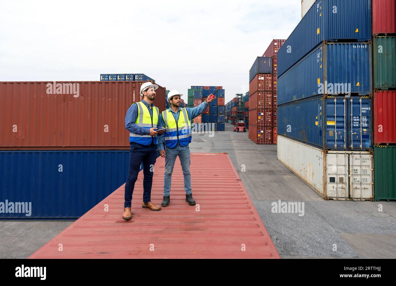 Der Transportmitarbeiter verwendet eine Walkie-Walkie, um auf den Lagerort des Containers zu verweisen. Erkläre dem Kollegen, wie die nächste Lieferung geplant ist. Junger Arbeiter mit sa Stockfoto