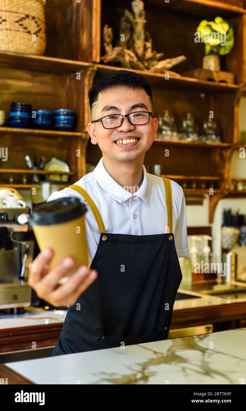 Vietnamesischer lächelnder Kellner hielt Pappbecher mit Kaffee in einem Café Stockfoto