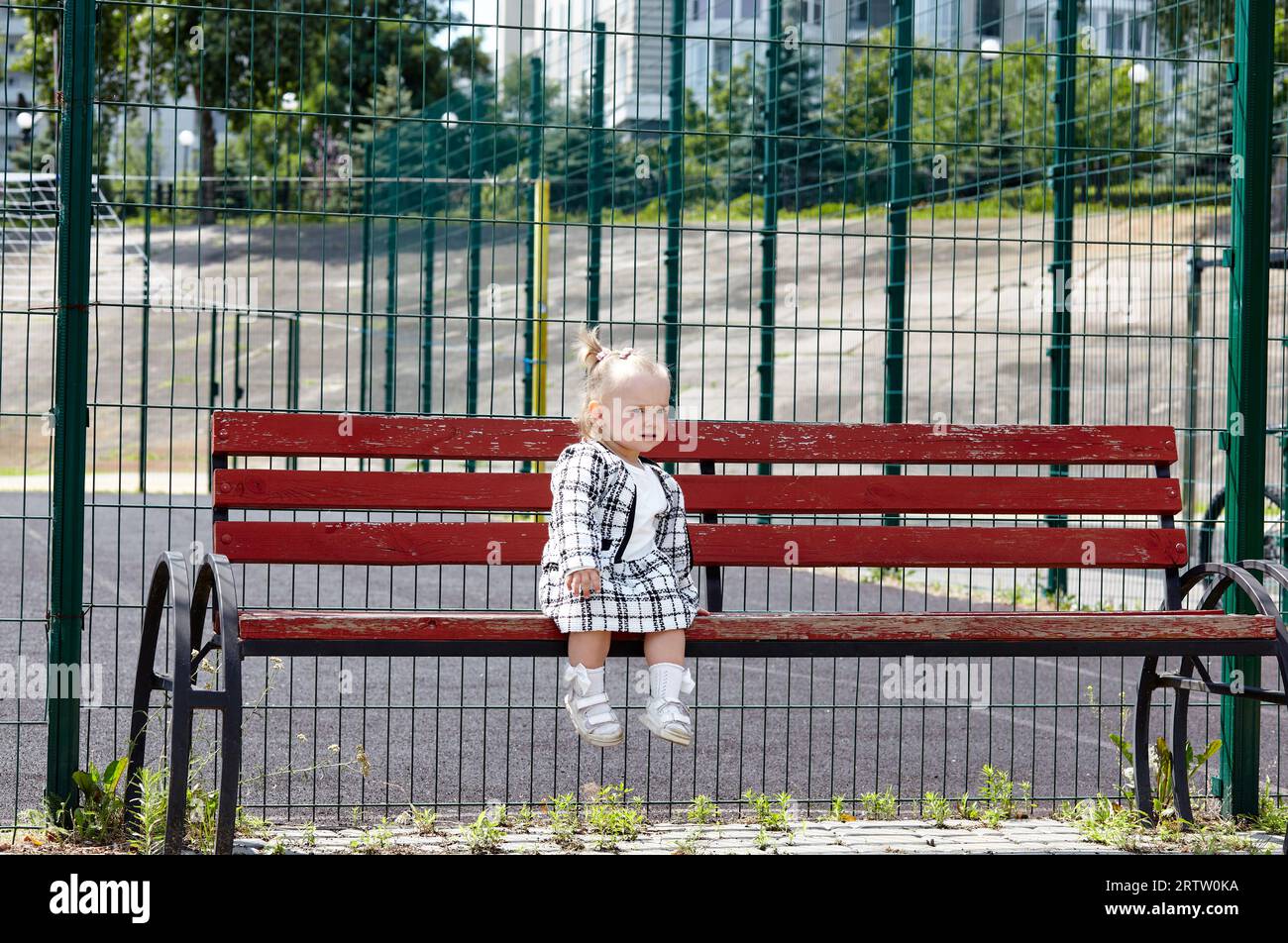Trauriges kleines Mädchen, das auf einer Bank sitzt und auf mom wartet. Kinderverlust im Stadtpark Stockfoto