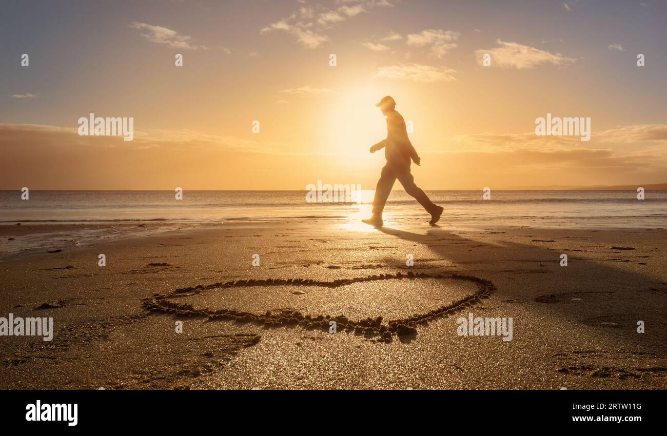 Leute, die bei Sonnenaufgang an einem Sandstrand spazieren gehen. Herzförmige Handzeichnung am Strand. Stockfoto