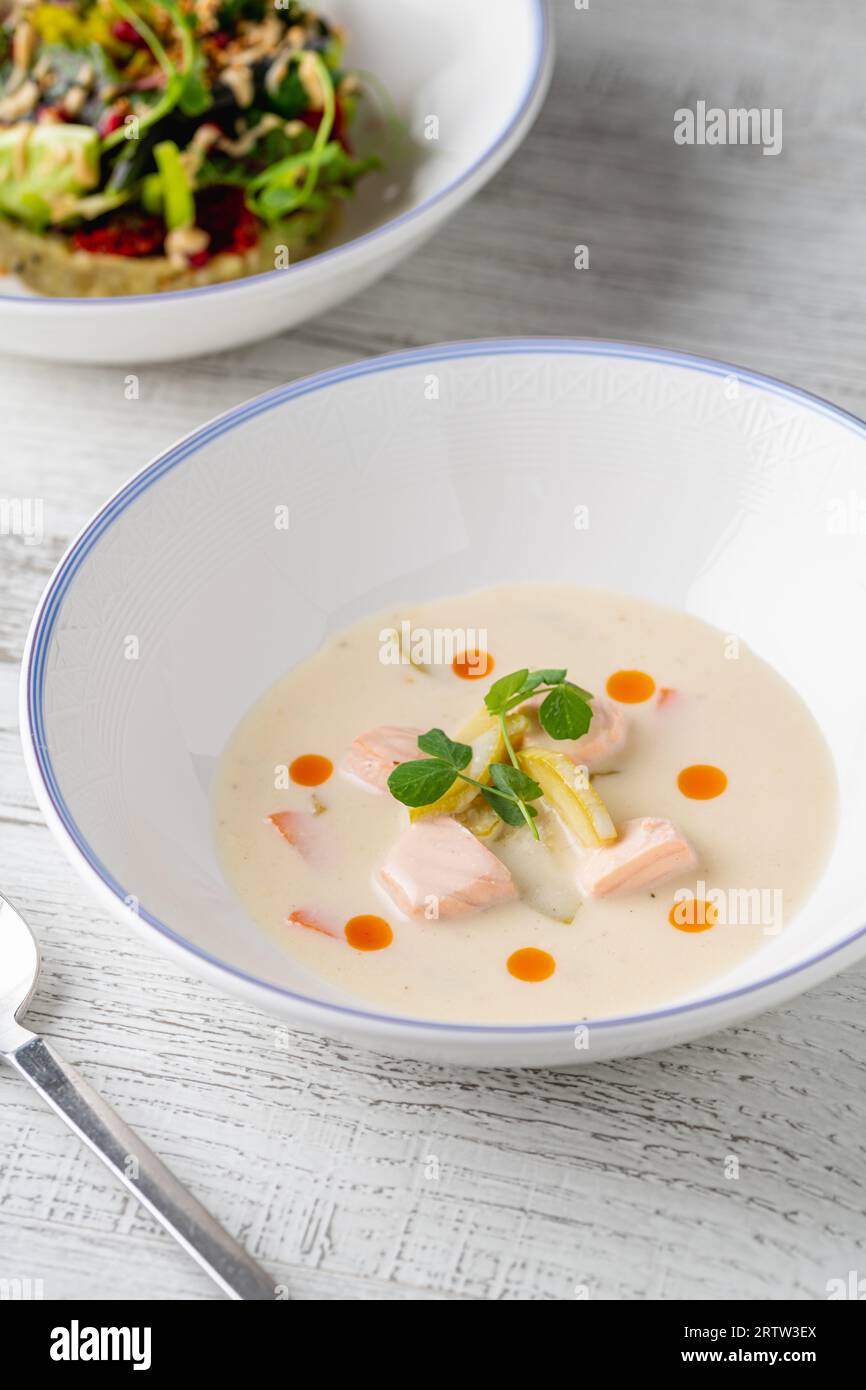 Lachssuppe auf einem weißen Porzellanteller mit Salat an der Seite Stockfoto
