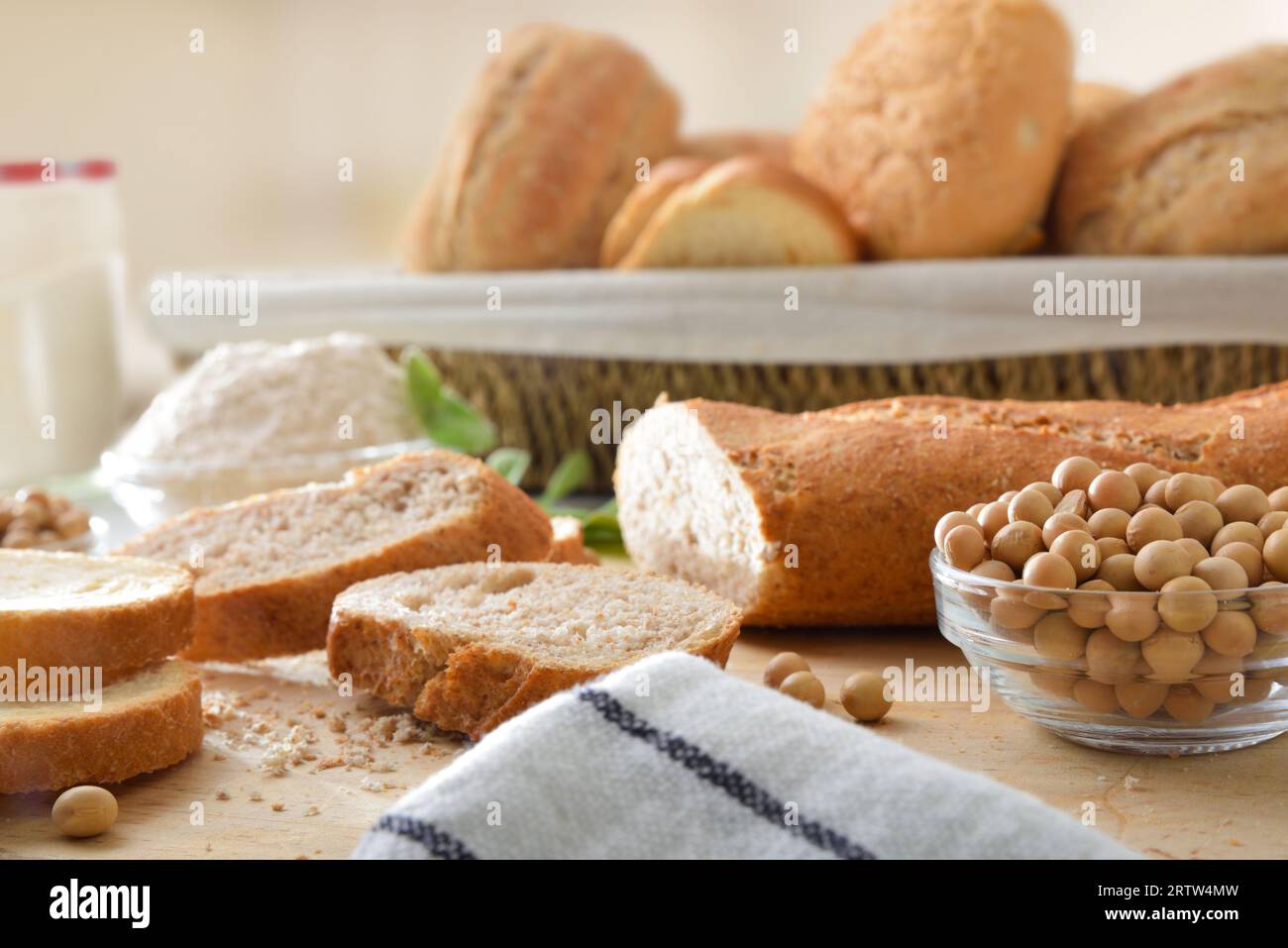 Sojabrot in Scheiben und Sojabohnen auf einem Schneidebrett mit Mehl und Brot in einem Korb im Hintergrund. Vorderansicht. Stockfoto