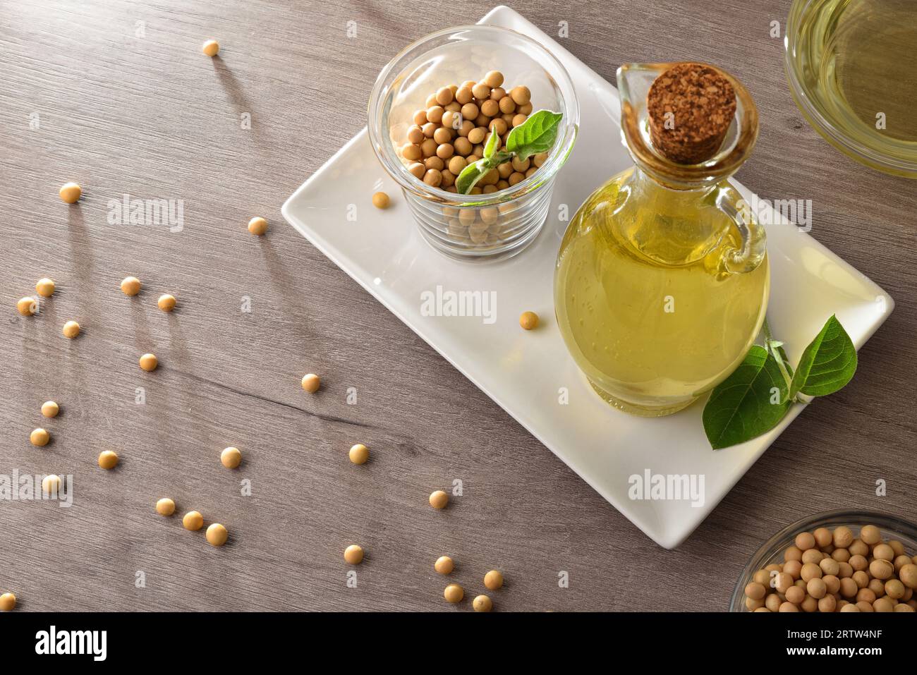 Sojabohnenöl in Glasflasche und trockene Sojabohnen auf weißem Teller auf Holztisch. Erhöhte Ansicht. Stockfoto