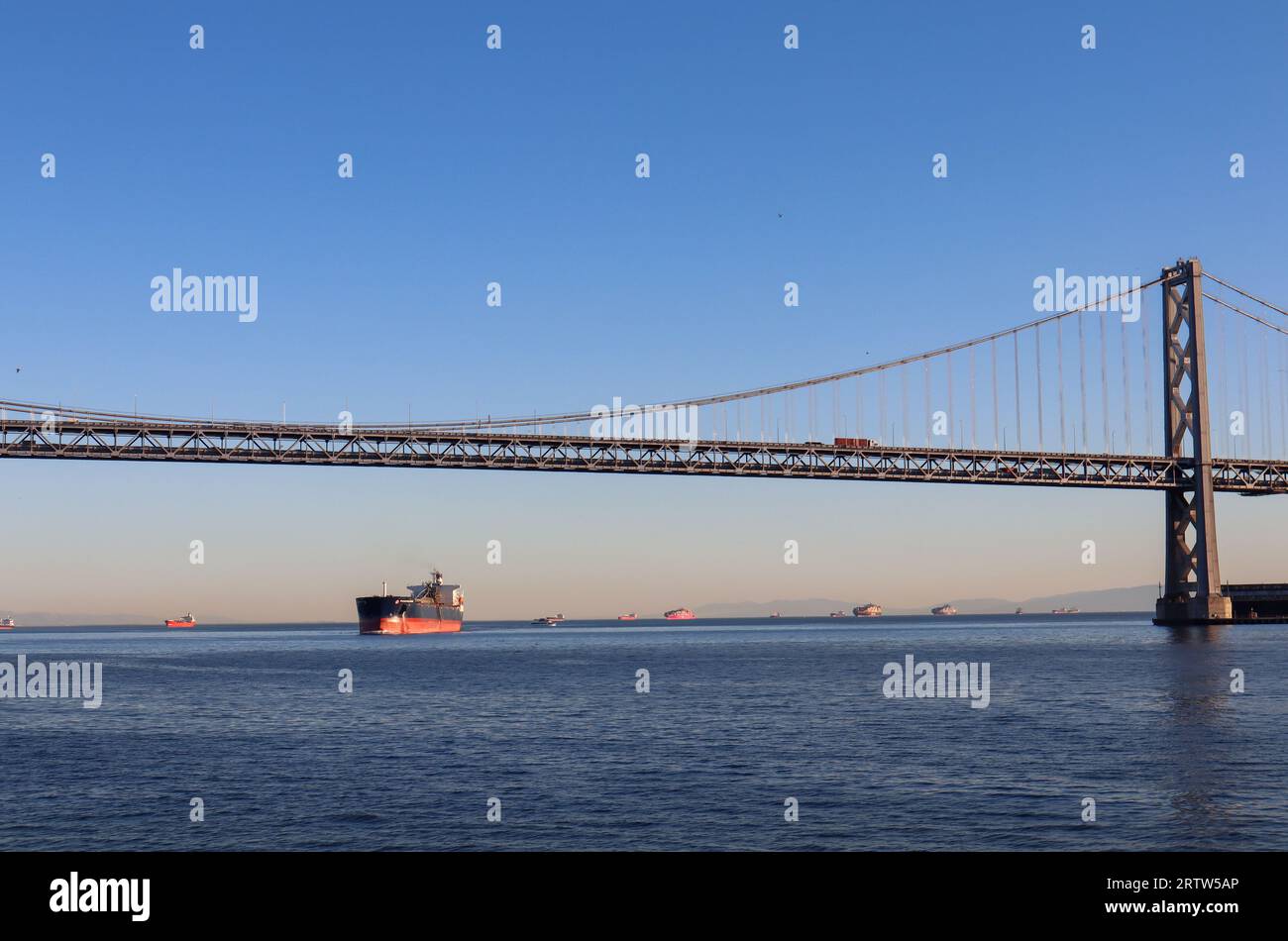 Blick auf die Bay Bridge vor blauem Himmel bei Sonnenuntergang, San Francisco, Kalifornien, USA. Bild, das mit Schiffen im Hintergrund aufgenommen wurde. Stockfoto