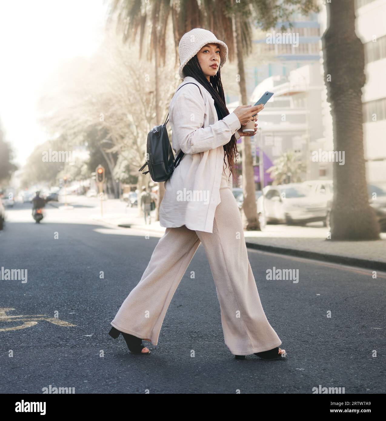 Frau, die mit dem Telefon die Straße überquert, in der Stadt spaziert und mit der Standort-App, sozialen Medien und Streetwear reist. Influencer, Streamer oder Gen z Girl mit Stockfoto