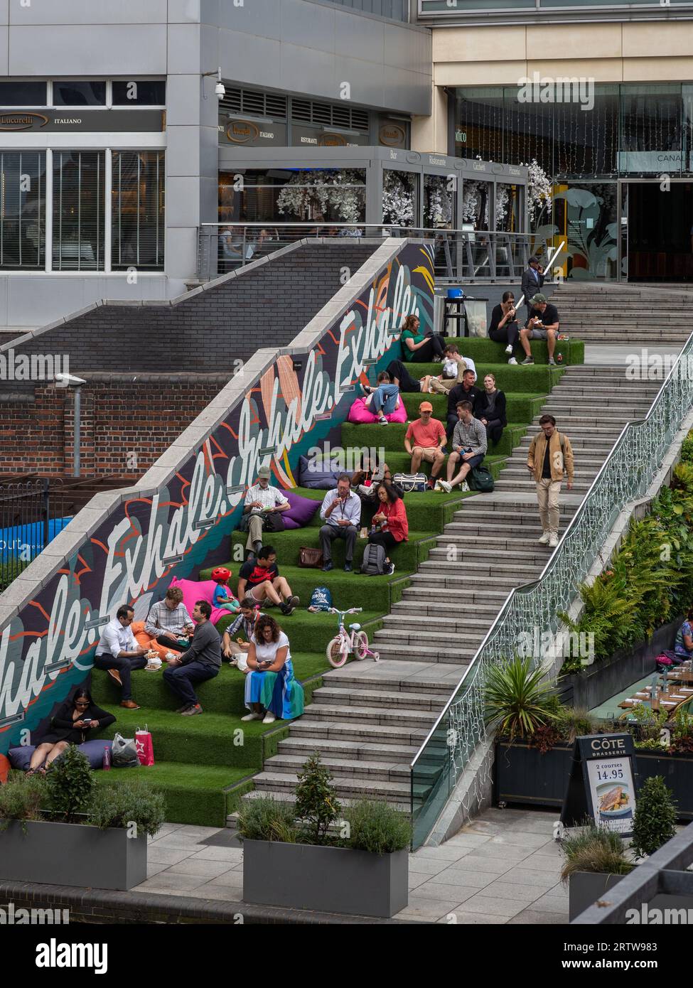 Leute, die im Freien essen, essen auf einigen grasbedeckten Stufen beim Mailbox-Gebäude, Birmingham, Großbritannien Stockfoto