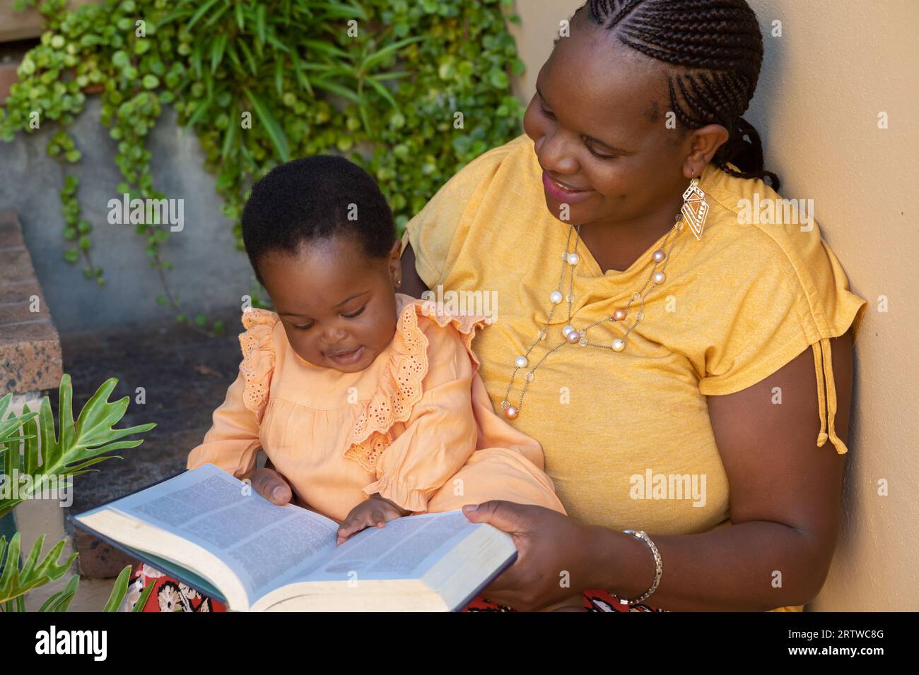 Porträt einer jungen schwarzen Mutter, die ihrer kleinen Tochter vorliest, die auf ihrem Schoß sitzt Stockfoto