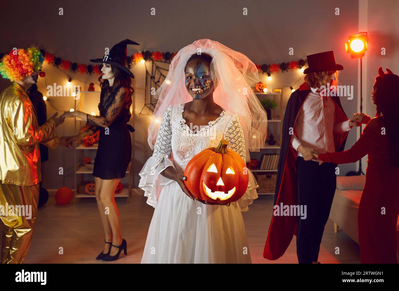 Glückliche schwarze Frau, die als tote Braut mit ihrer Jack-o-Laterne auf der Halloween-Party gekleidet ist Stockfoto