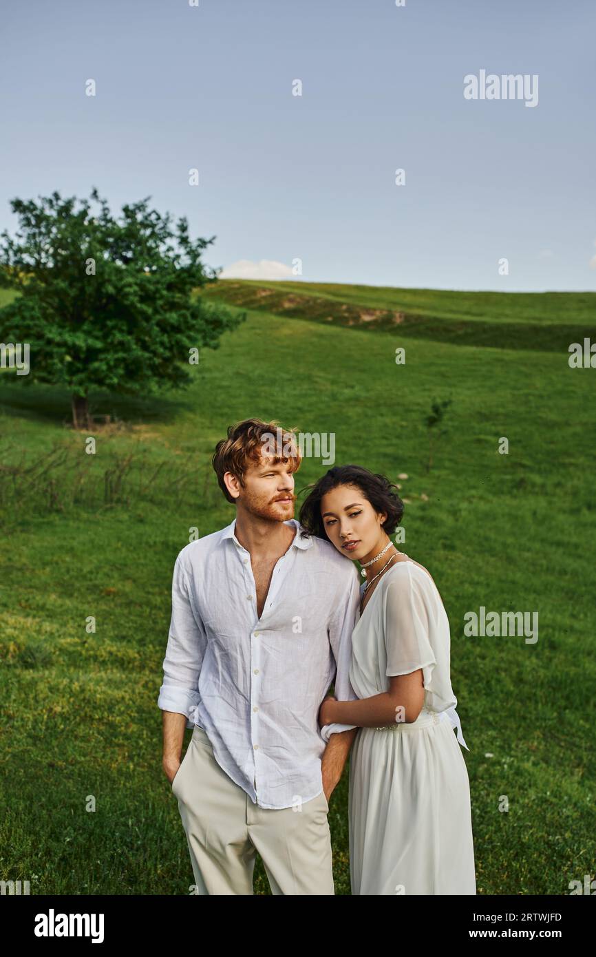 Die Verbindung zwischen Paaren, jungen, interrassischen Brautpaaren, die auf grünem Feld stehen, ist eine landschaftlich reizvolle Landschaft Stockfoto