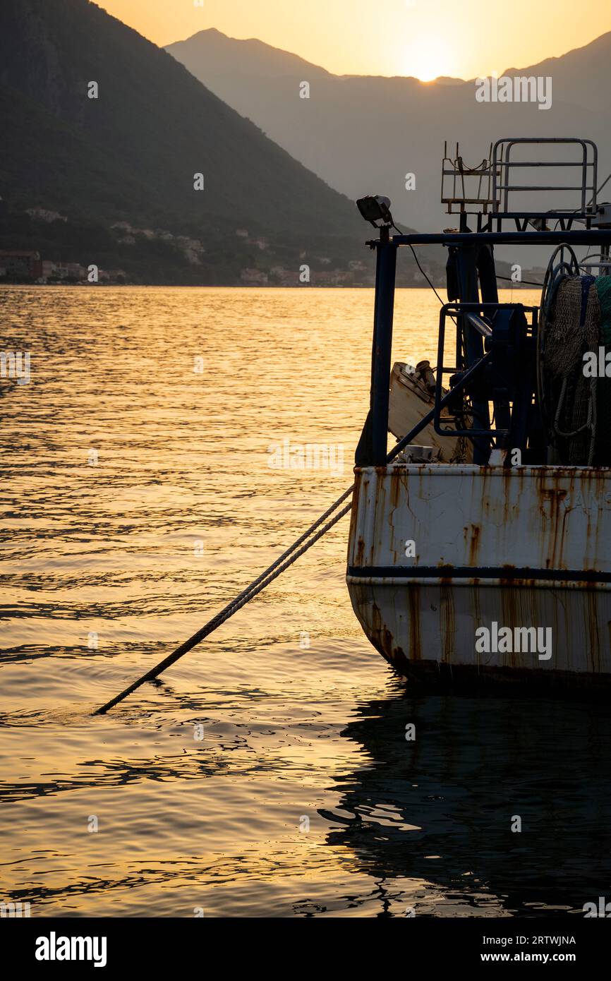 Ein altes, verwittertes, rostiges Fischerboot ankert bei Sonnenuntergang in der Bucht. Berge im Hintergrund. Stockfoto