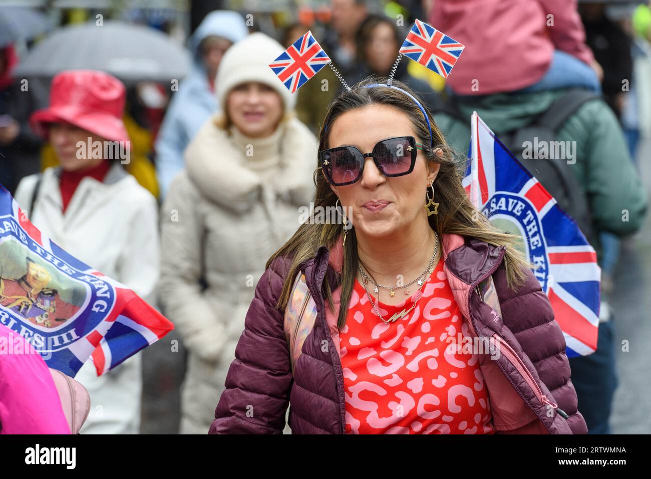 Eine Frau mit Union-Jack-Flaggen geht im Regen Piccadilly hinunter, ein Teil der großen Menschenmenge, die auf die Krönung von König Karl III. Zusteuert. Piccadilly, Stockfoto