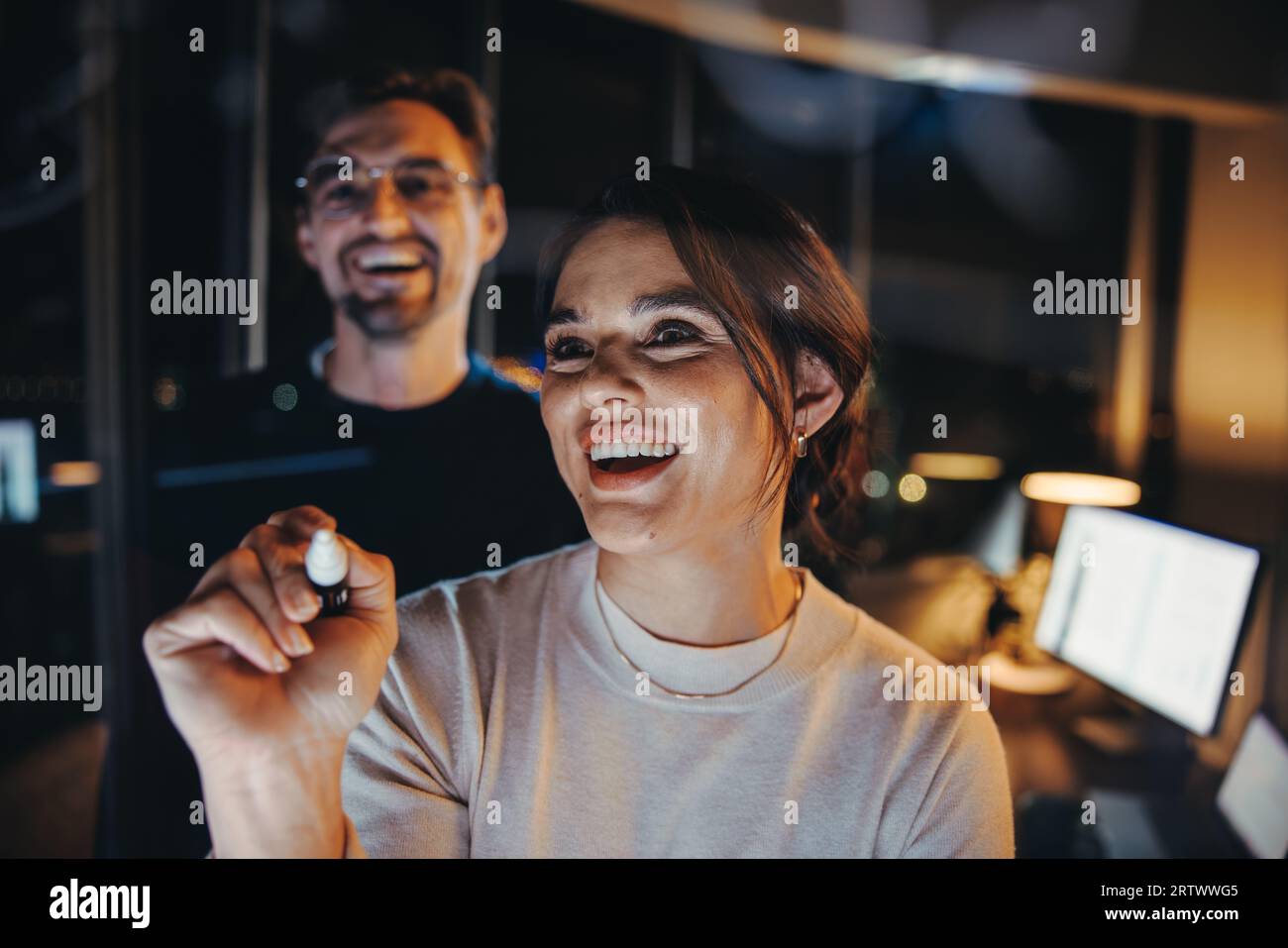 Zwei Geschäftsleute arbeiten in einem schwach beleuchteten Büro zusammen. Späte Arbeitszeiten und Teamarbeit fördern ihren Erfolg bei der Planung, Diskussion und beim Schreiben und fördern Stockfoto