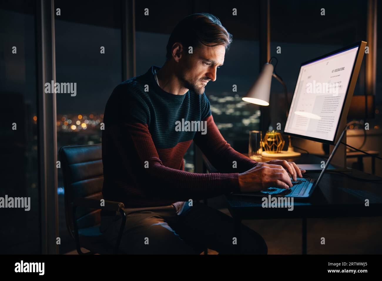 Professioneller kaukasischer Geschäftsmann, der spät in der Nacht in einem Büro arbeitet und auf seinem Laptop für ein digitales Marketingprojekt schreibt. Kreativer Unternehmer Stockfoto