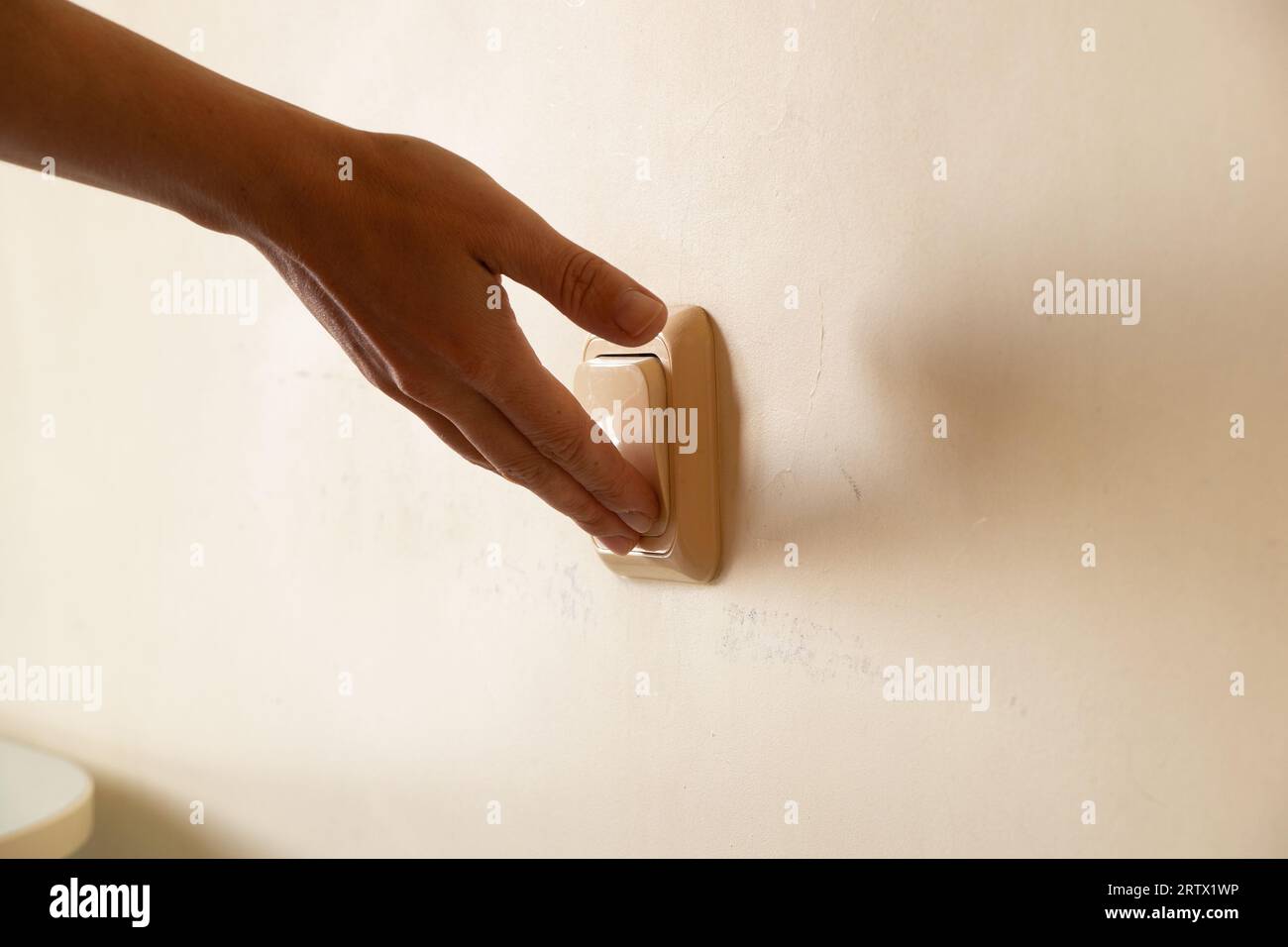 Die Hand einer Frau schaltet das Licht an der Wand in der Wohnung ein, den Schalter an der Wand, ein und aus Stockfoto