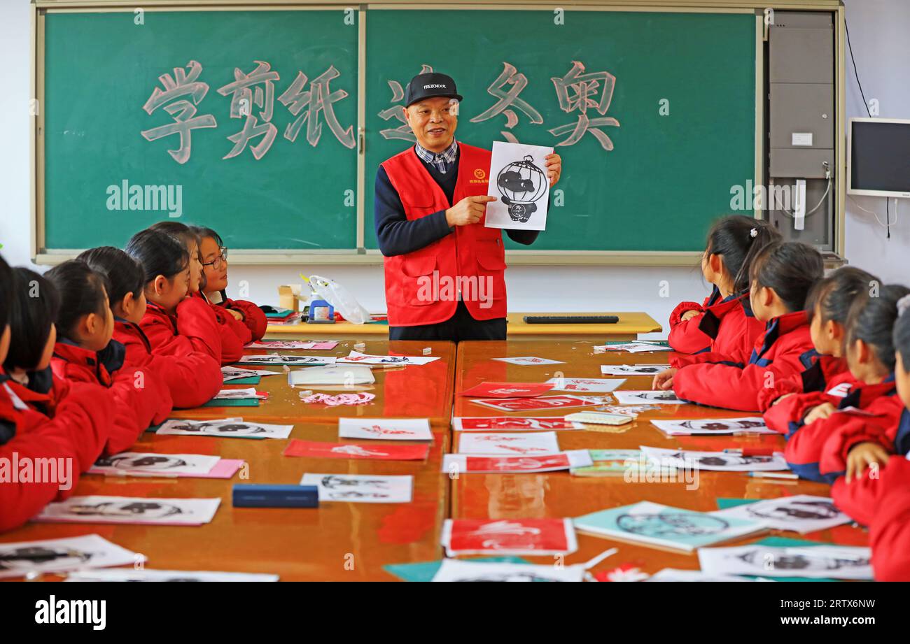 LUANNAN COUNTY, China - 10. Dezember 2021: Grundschüler lernen traditionelle chinesische Papierschneidekunst unter der Leitung von Lehrern, Nord-C Stockfoto