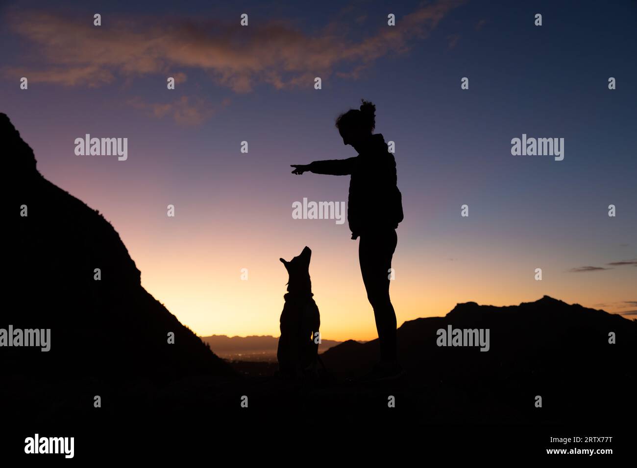 Junge Frau und ihr Hund auf einer Wanderung bei Sonnenaufgang in Silhouette Stockfoto