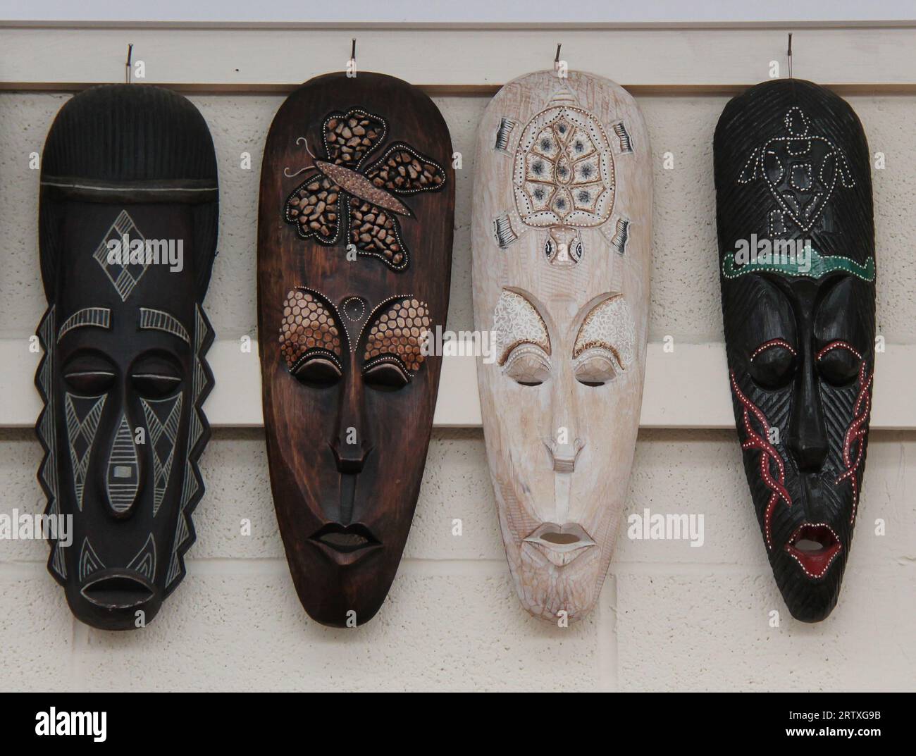 Vier verschiedene ethnische Holzmasken hängen auf dem Display. Stockfoto