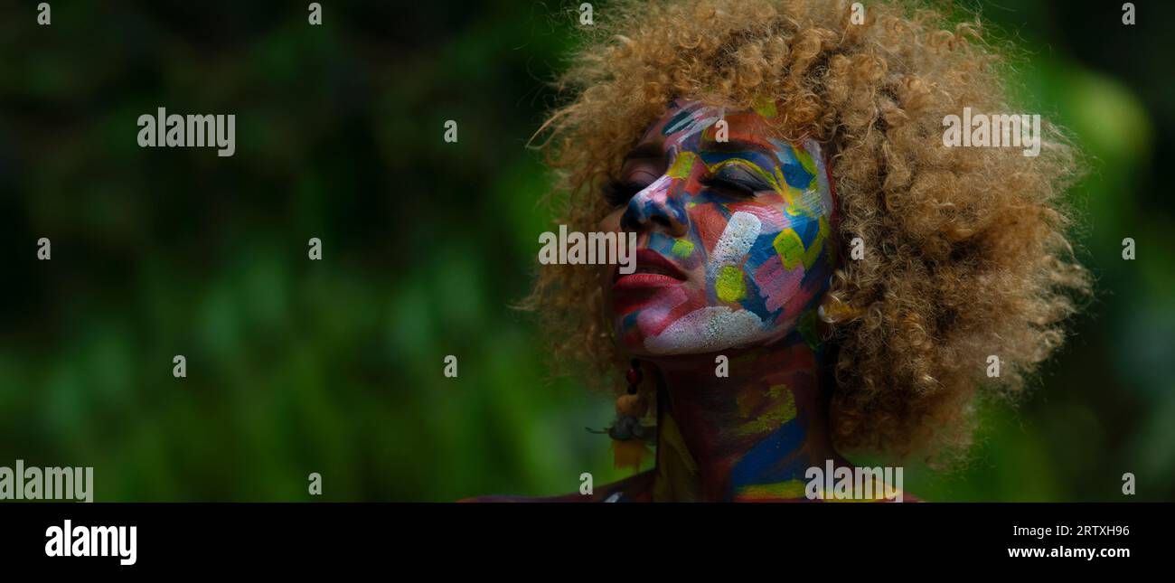 Nueva Loja, Sucumbios / Ecuador - 3. September 2020: Porträt einer jungen schwarzen Frau mit bunt bemaltem Gesicht mit geschlossenen Augen und entspanntem Ausdruck Stockfoto