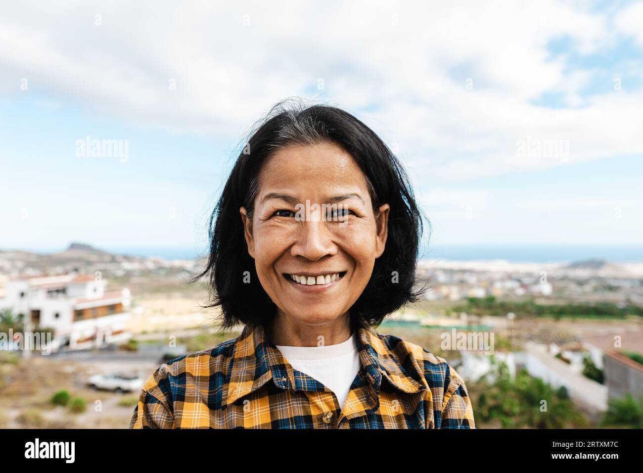 Glückliche Thai-Frau, die Spaß daran hat, auf dem Hausdach in die Kamera zu lächeln Stockfoto