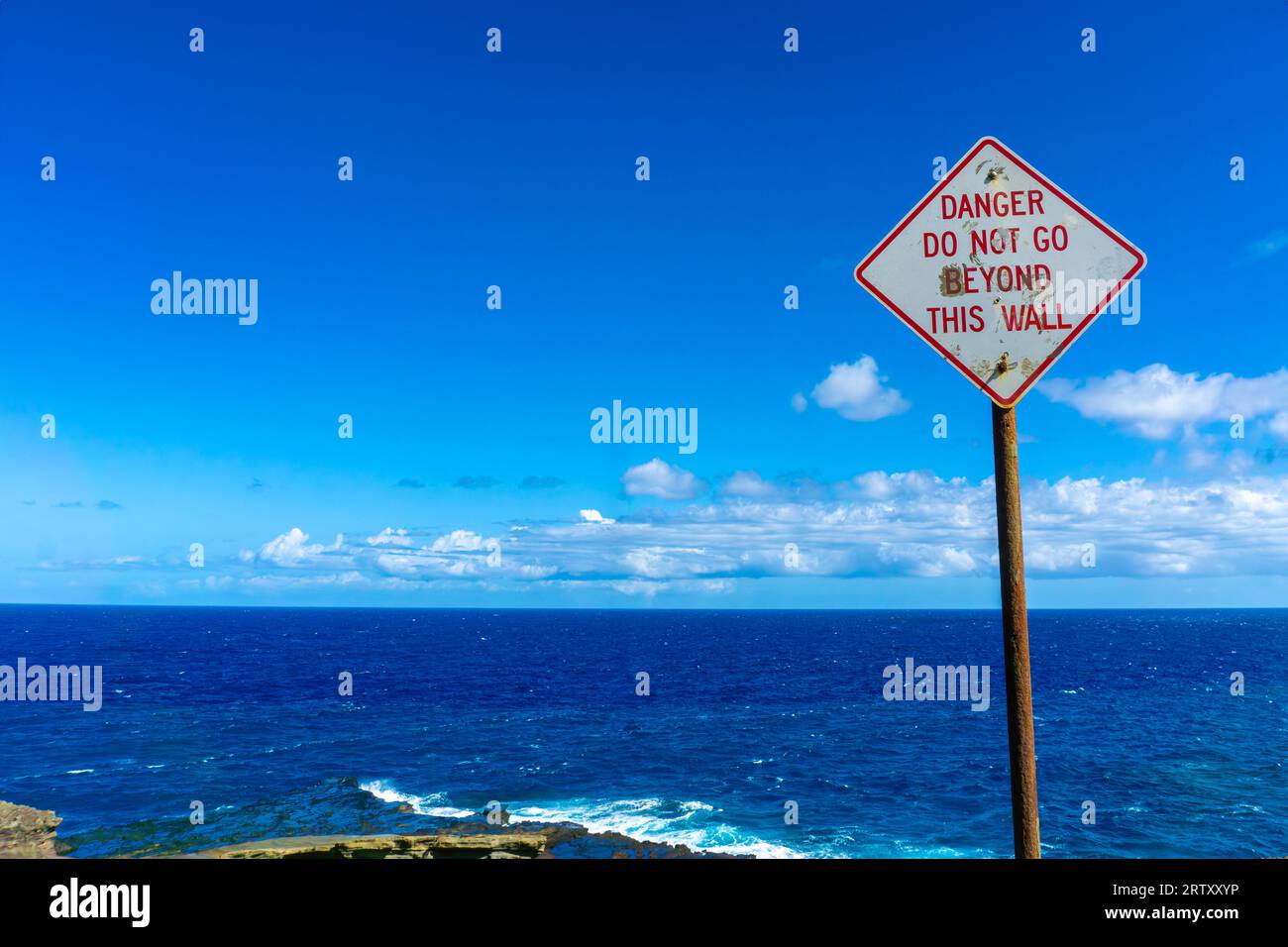 Warnschild hält Besucher am Lanai Lookout auf dem Kalanianaole Highway in Oahu, Hawaii, in Schach. Starke Wellen und Strömung des Pazifischen Ozeans am Rand Stockfoto