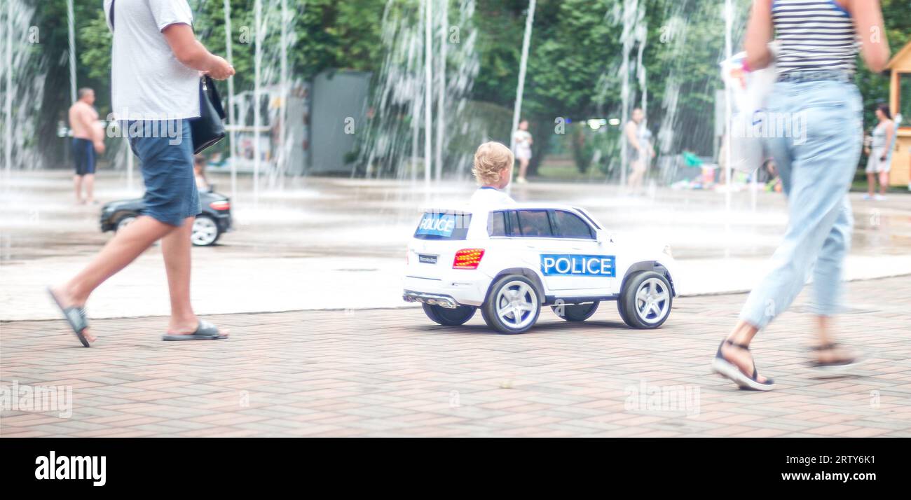 Die Familie reitet mit Kindern auf kleinen Elektroautos zwischen städtischen Brunnen Stockfoto