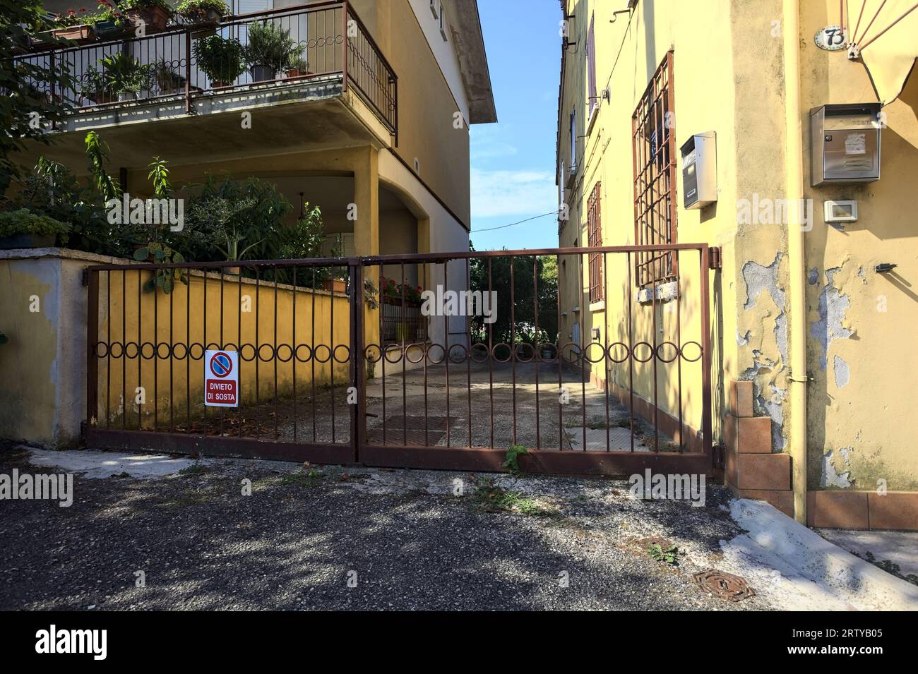 Einfahrtsweg zwischen zwei Häusern in einem italienischen Dorf auf dem Land tagsüber durch ein Tor blockiert Stockfoto