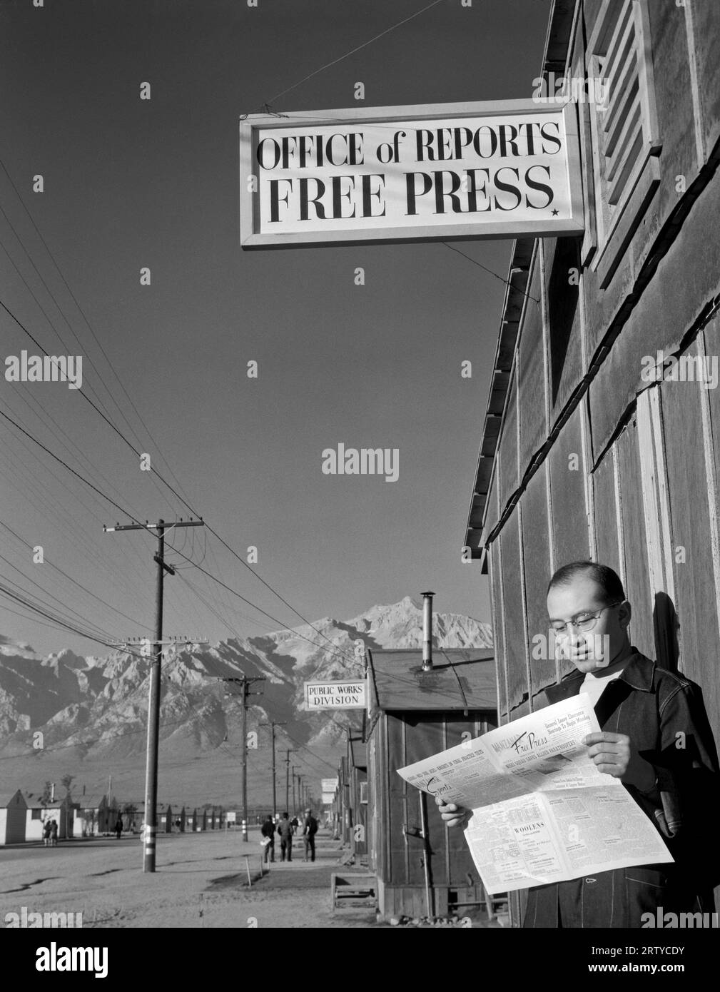 Owens Valley, Kalifornien 1943 Redakteur Roy Takeno las eine Kopie der Manzanar Free Press vor dem Zeitungsbüro im Manzanar war Relocation Center im Owens Valley, Kalifornien. Die Manzanar Free Press wurde im April 1942 von ehemaligen Journalisten ins Leben gerufen, die schließlich zu einem Umzugszentrum für Japaner wurden. In der ersten Ausgabe, die am 22. Juli 1942 gedruckt wurde, heißt es: „Wir möchten noch einmal wiederholen, dass die Freie Presse dem Volk von Manzanar gehört, dass sie nicht nur das Sprachrohr der Regierung ist, sondern die Meinung der Evakuierten in den s zum Ausdruck bringt Stockfoto