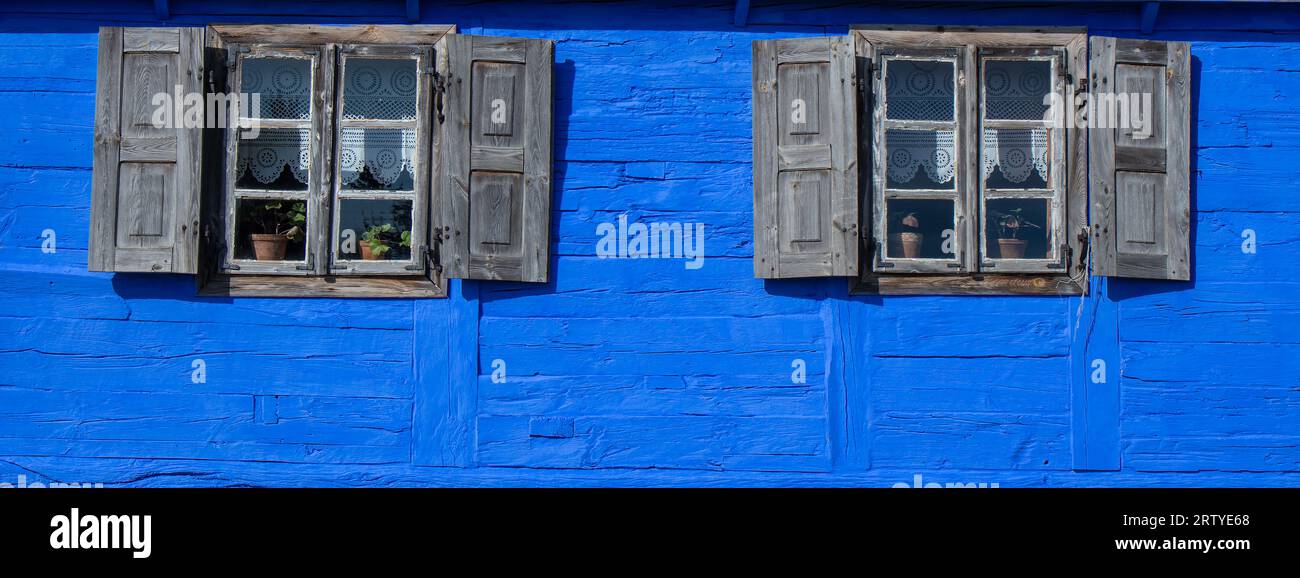Außenwand mit zwei Fenstern aus altem blauem Holzhaus Stockfoto
